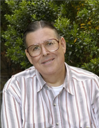 Paul Loiselle, a man wearing glasses, with short dark hair, wearing a striped shirt, smiling at the camera.